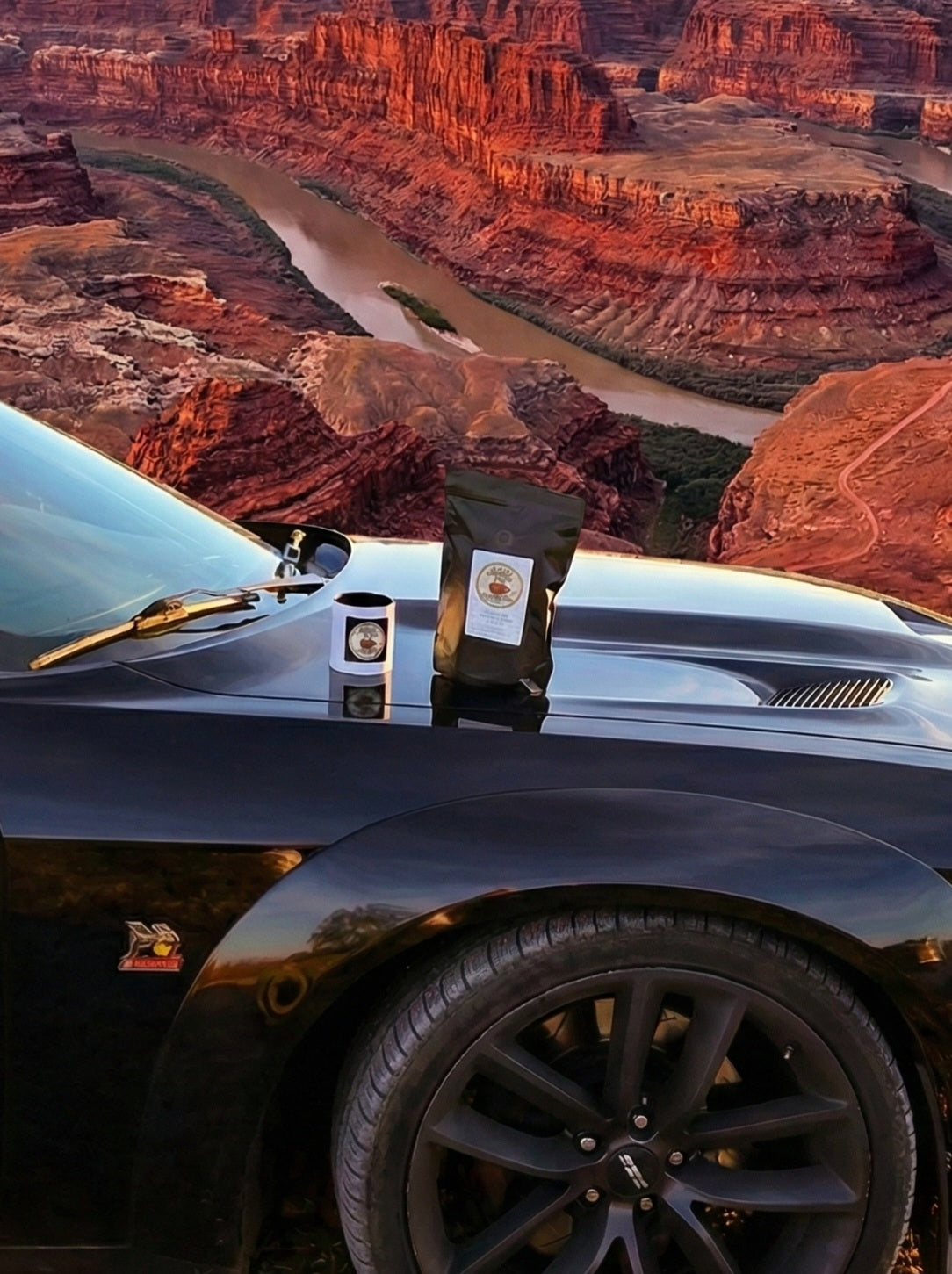 The Firm Ground Coffee bag and mug on a Dodge Challenger hood overlooking a desert canyon at sunset